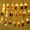 A string of lights with photos clipped to them, hanging in front of a white brick wall and white doors. Produktbild-Vorschau