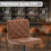 A close-up of a brown leather bar stool with a quilted diamond pattern on the seat and backrest, set against a blurred background of a bar or restaurant. Produktbild-Vorschau