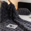 Dunkelgraue Kunstfell-Noppendecke, von Händen über einem Bett mit passendem Kissen hochgehalten Náhľad obrázku produktu