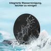 A black circular patient transfer disc is shown with water splashing around it, set against a blue sky and water background with rocks. Produktbild-Vorschau