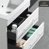 A close-up view of a white bathroom vanity with drawers open, revealing toiletries and storage compartments. Produktbild-Vorschau