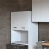 A white washing machine cabinet with two doors and an open shelf, placed in front of a tiled wall. Produktbild-Vorschau