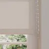 A close-up view of a beige roller blind with a beaded pull cord, seen from the side, with a window and greenery visible through the bottom. Produktbild-Vorschau