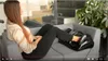 A woman is using a foot massager while sitting on a couch. Náhľad obrázku produktu