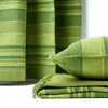 A close-up view of green striped curtains and matching decorative pillows and a folded throw blanket. Náhled obrázku produktu