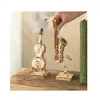 A hand holding a wooden saxophone model above a wooden violin model and a small wooden stand, all on a wooden surface. Anteprima dell’immagine prodotto