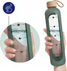 A hand holding a green glass water bottle with time markings and a bamboo lid. A close-up inset shows the water level and markings. Voir les images du produit