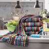 A stack of colorful kitchen towels is displayed on a kitchen counter next to a bowl of lettuce and some kitchen utensils. Produktbild-Vorschau