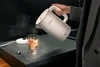 A person pours hot water from a white electric kettle into a glass. Produktbild-Vorschau