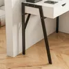 A close-up view of the legs and drawer of a white desk with black metal legs, set against a white wall and a wooden floor. Náhled obrázku produktu
