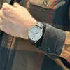A close-up shot of a man's wrist wearing a watch, with his hand resting on his other arm, wearing a plaid shirt. Náhľad obrázku produktu
