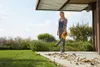 A woman is using a leaf blower to clear leaves from a wooden deck and lawn. Produktbild-Vorschau
