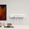 A white power strip with multiple outlets and plugs is mounted on a light gray wall above a desk with headphones and a mouse. Náhled obrázku produktu