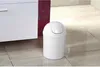 A white plastic trash can with a flip-top lid sits on a tiled floor next to a white cabinet. Náhled obrázku produktu