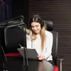 A woman in a recording studio wearing headphones and looking at a clipboard. Produktbild-Vorschau