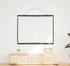 A white projection screen is hanging on a white wall above a light wood cabinet with a small plant and a storage box on top. Náhled obrázku produktu