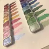 A set of watercolor paints with swatches of color on paper. Voir les images du produit