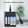 A black battery charger with four slots, holding two AAA and two AA rechargeable batteries, is plugged into a USB port. A green plant is visible in the background. Podgląd zdjęcia produktu