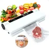 A vacuum sealer machine is shown with a variety of fresh fruits and vegetables in the background, and a piece of raw meat being vacuum-sealed in the foreground. Produktbild-Vorschau