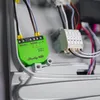 A close-up view of a green Shelly DALI Dimmer Gen3 device with wires connected, installed inside a gray electrical enclosure. Produktbild-Vorschau