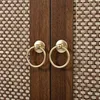 A close-up view of two brass ring handles on wooden cabinet doors with woven rattan panels. Anteprima dell’immagine prodotto