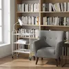 A white serving cart with three shelves is placed next to a gray armchair in a room with bookshelves. Voir les images du produit