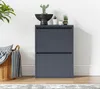 A dark gray shoe cabinet with two flip-down doors is shown in a room with a basket of blankets and plants on top. Produktbild-Vorschau