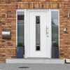 A white front door with a glass panel featuring a heart design, flanked by two windows and set against a brick wall. A mailbox is mounted to the left of the door, and two potted plants are on either side of the steps leading to the door. Anteprima dell’immagine prodotto