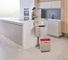 A modern kitchen with a woman in the background and a multi-compartment recycling bin in the foreground. Podgląd zdjęcia produktu