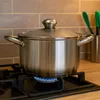 A stainless steel pot with a glass lid is placed on a gas stove with a blue flame visible. Produktbild-Vorschau