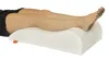 A person's legs are resting on a white leg elevation pillow. Produktbild-Vorschau
