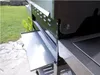 A close-up view of a grill's side shelf and ventilation system, with a grassy yard in the background. Podgląd zdjęcia produktu