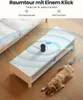A security camera is shown on a coffee table in a living room with a dog lying on the floor. Produktbild-Vorschau