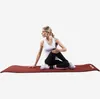 A woman is performing a yoga pose on a dark red yoga mat. Náhľad obrázku produktu