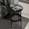 A black round side table with a magazine and a cup of coffee on it, next to a gray sofa. Náhled obrázku produktu