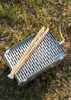 A grill and tongs are placed on grass and dirt. Produktbild-Vorschau