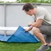 A man is kneeling on the grass, holding a blue tarp next to an above-ground swimming pool. Produktbild-Vorschau