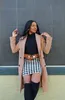 A woman posing in front of a textured wall, wearing a coat, skirt, and boots. Produktbild-Vorschau