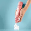 A hand holding a pink hair product bottle and dispensing foam. Voir les images du produit