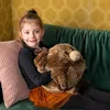 A young girl is sitting on a couch, hugging a large stuffed reindeer toy. Anteprima dell’immagine prodotto