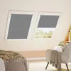 A bedroom scene with two slanted windows covered by gray pleated blinds. A bed with a textured throw is on the left, and an armchair with a blanket is on the right. Produktbild-Vorschau