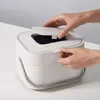 Hands opening the lid of a white compost bin on a table. Voir les images du produit