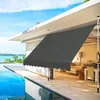 An outdoor patio area with a swimming pool and a modern house, featuring a gray retractable awning. Podgląd zdjęcia produktu