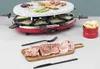 A red raclette grill with a stone top, set up with food and utensils on a table. Produktbild-Vorschau
