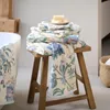 A stack of floral patterned towels on a wooden stool next to a bathtub. Produktbild-Vorschau