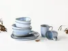A set of blue ceramic dishes and mugs arranged on a white surface, with dried plant sprigs on either side. Náhľad obrázku produktu
