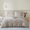 A neatly made bed with taupe bedding and two pillows, a white throw blanket, and a book on the bed. A floor lamp is on the left, and a nightstand with a deer figurine and a cup is on the right. Podgląd zdjęcia produktu