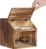 A hand is shown closing the lid of a wooden suggestion box with a clear front panel. Náhled obrázku produktu
