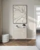 A minimalist room with a modern chest of drawers, a pouf, and abstract art. Produktbild-Vorschau