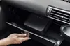 A hand is opening a car's glove compartment to reveal a black air compressor inside. Produktbild-Vorschau